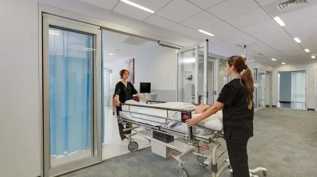 A hospital bed wheeled out of a set of doors.