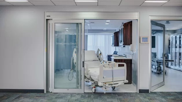 A set of sliding doors in a hospital room with a bed coming through the doors.