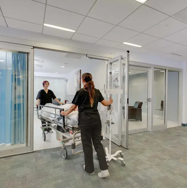 A hospital bed wheeled out of a set of doors.