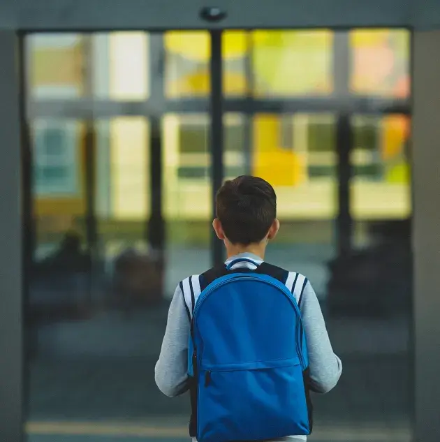 young boy in backpack standing in front of doors