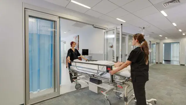 A hospital bed wheeled out of a set of doors.