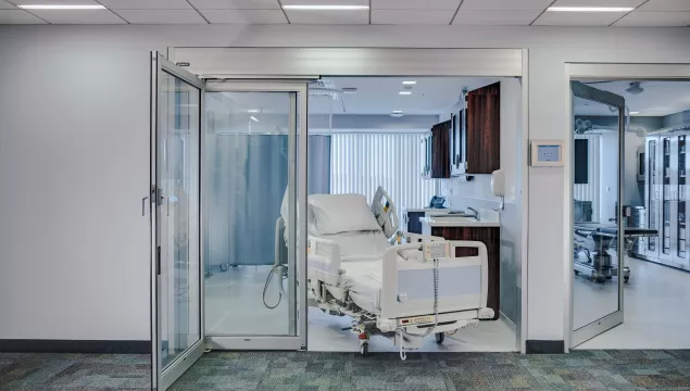 A set of sliding doors in a hospital room with a bed coming through the doors.