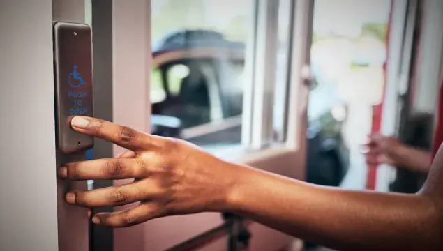 person pressing activation push plate on a drive thru door